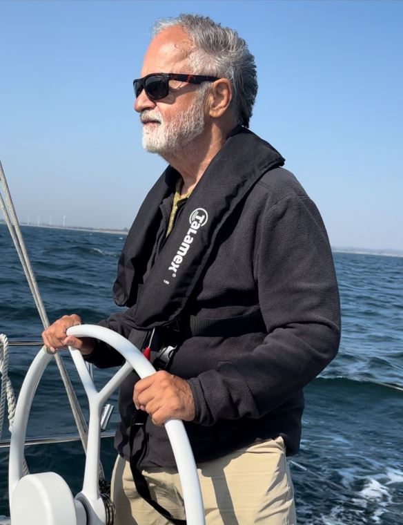 David E. Reed sailing a boat, wearing sunglasses and a life jacket.